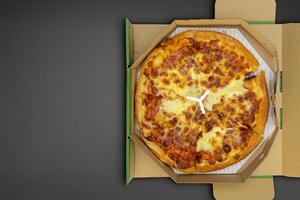 Pizza in a cardboard box on a black chalkboard background. Space for text. photo