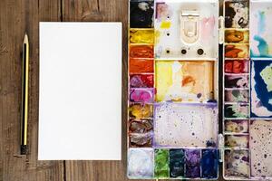 color in the palette water paints. A blank drawing paper and a pencil are placed on the side. photo