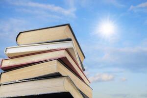 Stack Of Books Against Blue Sky. The sky is full of clouds floating around, both small and large, the sun is shining brightly photo