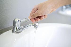 Image of hand closing valve on sink in bathroom. Water dripping to stop running as hand turn off the faucet photo
