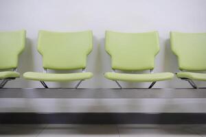 Row of green office chairs standing in corridor or conference room, empty dark seats arranged in line in boardroom, range of basic stools in front of white wall. Interview, recruitment concept photo