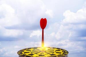 Red dart arrow hit in the target center of dartboard with sky background photo