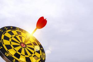 Red dart arrow hit in the target center of dartboard with sky background photo