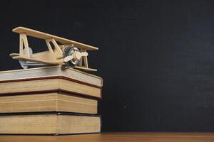 The books that are stacked and Plane model placed on the table. The background is a blackboard, Back to school concept. photo