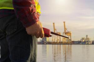 Closeup hand caucasian men foreman is talking with colleague by using walkie talkie and standing in front of industrial containers. Engineering and Technology concept photo