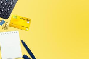 Flat lay or top view of blue pen, Notebook, Credit card with calculator on vivid yellow background photo