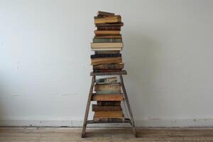 Tall stack of old books resting on wooden ladder photo