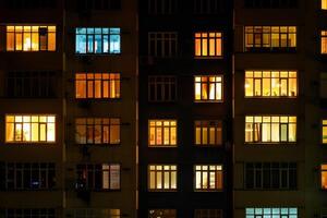 Facade of apartment building at night showing life inside through lit windows photo