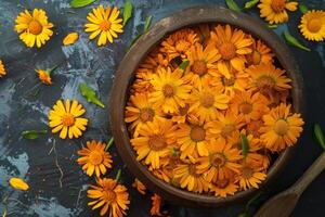 Fresh calendula flowers lying in a clay bowl on a dark background photo