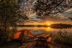 Orange tent and picnic table illuminated by setting sun at lakeside campsite photo