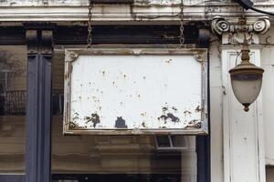 Old weathered rusty empty shop sign hanging on a building facade photo