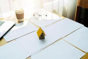 The model of the house is placed on a document with a laptop on the desk photo