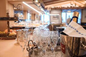 Dining or banquet area indoors with empty wine glasses on table, champagne bottle in ice bucket with blue embroidery cloth, warm lighting, buffet setup. photo