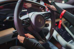 Close up view of Porsche steering wheel with modern design and multifunction buttons. Driver's hands with red nails on wheel. Red seatbelt, sleek dashboard. photo
