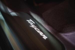 Close up of a Taycan branding element on a vehicle, hinting at luxury and high performance. Dark background, carbon fiber texture. photo