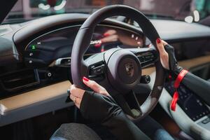 Close up view of Porsche steering wheel with modern design and multifunction buttons. Driver's hands with red nails on wheel. Red seatbelt, sleek dashboard. photo