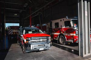 Fire station garage with red and white Chevrolet truck from Colorado at the forefront, ready for deployment. Sparks Fire Rescue fire engine parked in the background. Urban setting. photo