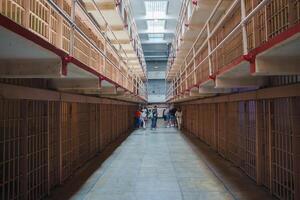 Interior view of Alcatraz prison in San Francisco, USA. Long corridor with two levels of cells, barred doors, red handrails. Visitors on guided tour, historical atmosphere. photo