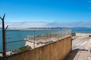 Alcatraz prison view in San Francisco, USA. Picture shows outdoor area with chain link fences and bay view. Golden Gate Bridge covered by fog in background. photo