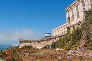 Alcatraz Island view in San Francisco Bay, USA, featuring the historic prison building with barred windows, surrounding vegetation, and clear sunny sky. photo