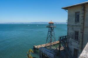 View from Alcatraz prison, San Francisco, USA. Weathered building with barred windows on the right, guard tower with searchlight on left. Rustic, historical site by the Bay. photo