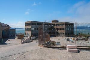 Scene showing the abandoned Alcatraz prison in San Francisco, USA. The fenced outdoor area and dilapidated building evoke a sense of isolation and history. photo
