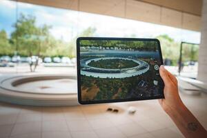 Hand holding tablet displaying Apple Park Headquarters in Cupertino, California. Iconic circular building known as spaceship visible. Person in building admiring design. photo