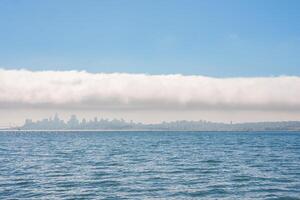 Discover the serene San Francisco skyline shrouded in low lying clouds, reflected in calm waters, under a clear sky. Iconic landmarks await in this picturesque cityscape. photo