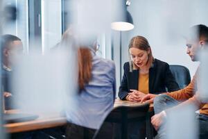 In a sleek glass office space, a team of business professionals engage in lively discussions and exchange strategic ideas, showcasing collaboration and innovation at the heart of modern corporate photo