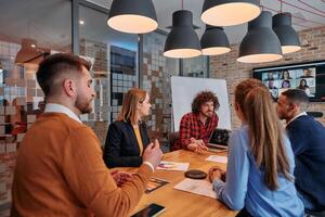 In the vibrant ambiance of a modern startup office, a diverse team of business professionals engage in discussions on various projects and develop new business strategies, epitomizing creativity and photo
