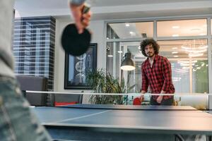 Business colleagues take a break from work to enjoy a game of table tennis, fostering teamwork and camaraderie in the workplace photo