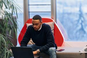 Overtime working. African American man with closed eyes is resting at work at laptop. Tired male programmer taking a break due to overtime work. photo