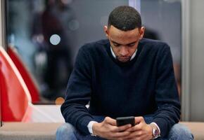 Young African American work in coworking space using smartphone analyzing online market trends, focused man worker reading financial news or browsing internet on phone. Technology concept photo