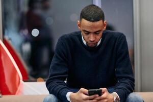 Young African American work in coworking space using smartphone analyzing online market trends, focused man worker reading financial news or browsing internet on phone. Technology concept photo