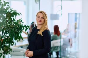 Portrait of a Blonde Businesswoman in a Modern Office with Her Workspace and Colleagues in the Background. photo