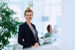 Portrait of a Blonde Businesswoman in a Modern Office with Her Workspace and Colleagues in the Background. photo