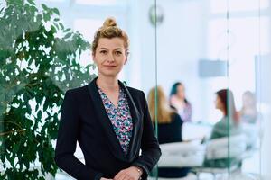 Portrait of a Blonde Businesswoman in a Modern Office with Her Workspace and Colleagues in the Background. photo