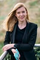 Blonde Businesswoman in Black Suit Using Smartphone on Break in Modern Urban Environment. photo