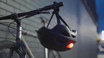 Topic of road safety for cyclist. A bicycle helmet with red light beacon hangs on handlebars of a bike in the evening in the city. Flashing red bicycle safety light. Helmet with red lamp at night video