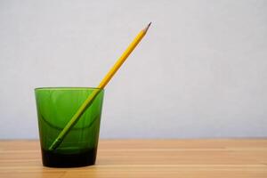 Yellow wooden pencil in green glass isolated on white background Work-from-home banner idea WFH with copy space for text that runs or wraps around. photo