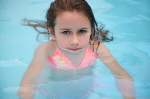 Young girl swimming in pool, looking at camera with serious expression photo