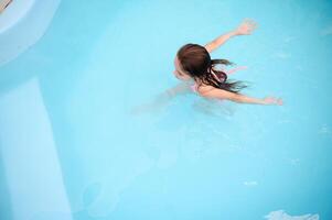 Young girl swimming in a pool, enjoying a summer day with open arms photo