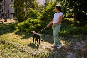 Woman walking her dog on a sunny day in a park with green trees and grass photo