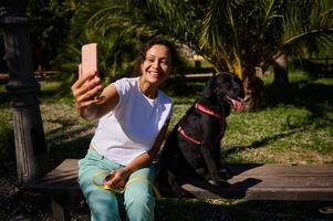 Woman taking selfie with happy black dog in park on sunny day photo