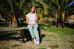 Woman enjoying phone conversation while sitting on park bench with her dog on a sunny day photo