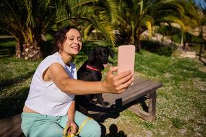 Woman taking selfie with her dog in a sunny park, capturing a happy moment together photo