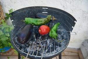 Grill with fresh vegetables including eggplants, chili peppers, and tomato on the barbecue photo