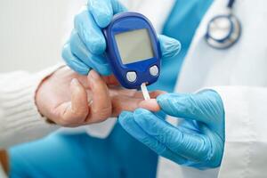 Asian doctor using digital glucose meter for check sample blood sugar level to treatment diabetes. photo