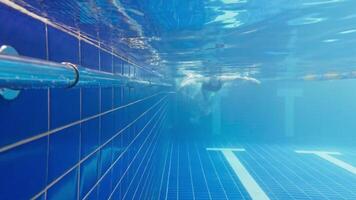 Under water view of professional female swimmer. Woman athlete swimmer training at swimming pool. Underwater view woman dives in pool. Underwater view of girl diving gliding underwater with bubbles video