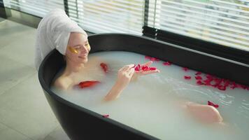 Spa relaxation. Woman lying in bath with red roses petals. Girl relaxing in bathroom at home. Pretty female enjoying taking hot bath. Stress relief. Rest after hard working day video